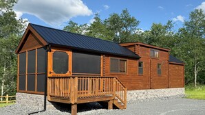 A wooden cabin with a metal roof, a wooden deck, and a stone foundation.