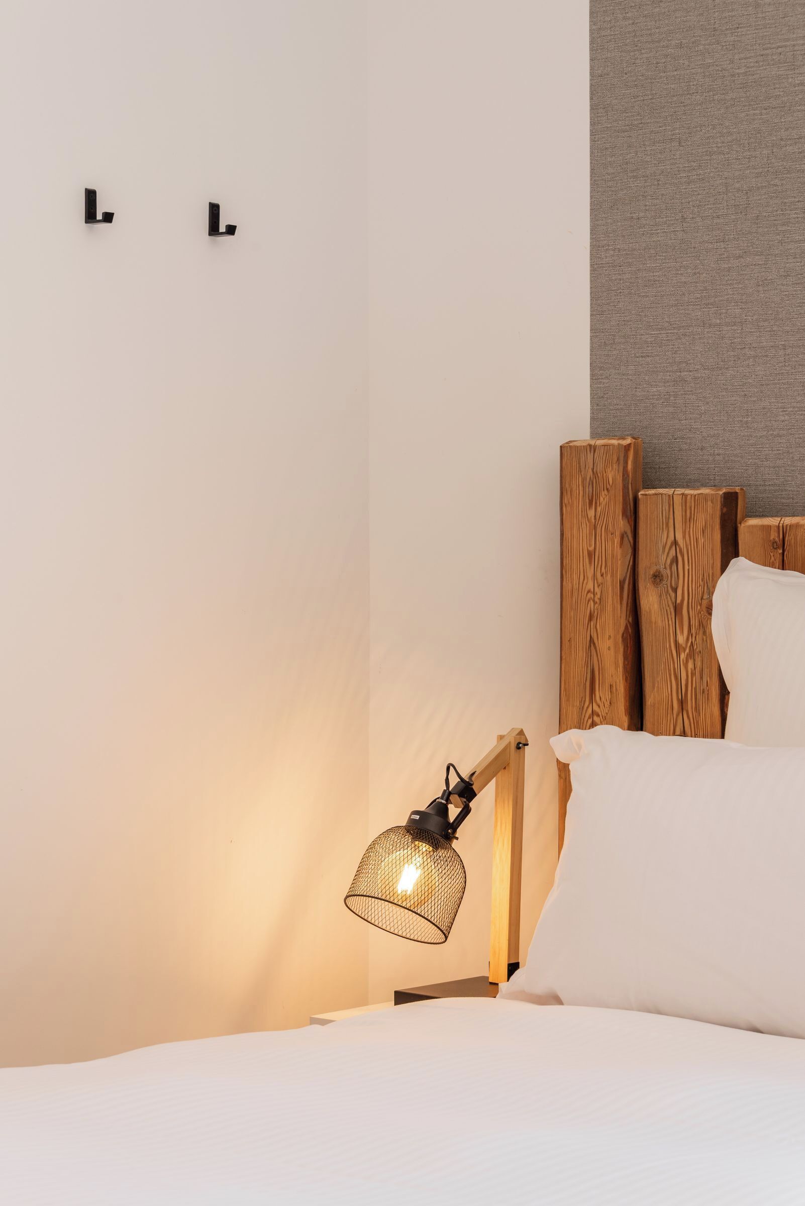 Een netjes opgemaakt bed met witte lakens, een houten hoofdbord en een enkele bedlamp met een metalen kap.