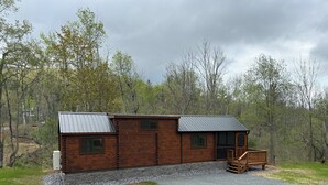 A log cabin with a metal roof, a porch with a wooden railing, and a stone foundation. - Tiny Cabin #5 by Windham NY Escape 'Scenic Stay' (Hensonville)
