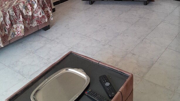 A hotel room with a bed, a TV on a stand, a coffee table with a tray, remote controls, and a thermostat. - 10 m walk from the sea, lovely apartment for rent, ideal for families (Annaba)