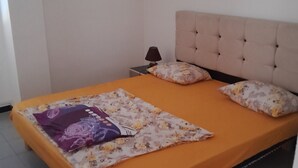 A bed with an orange bedspread and floral-patterned pillows, a bedside lamp, and a tufted headboard. - 10 m walk from the sea, lovely apartment for rent, ideal for families (Annaba)