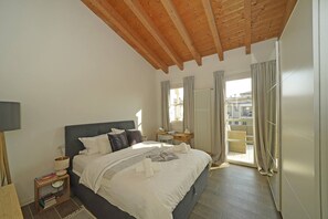 A bedroom with a large bed, a bedside table with a lamp, a small side table, and a view of the outside through a window. - Corte Fasanella 48 (Toscolano-Maderno)