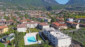 A residential area with modern apartment buildings, a swimming pool, and a mountainous backdrop. - Corte Fasanella 48 (Toscolano-Maderno)