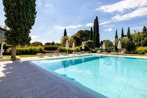 A rectangular swimming pool with clear blue water, surrounded by a tiled deck. There are lounge chairs and umbrellas along the poolside. - Corte Fasanella 48 (Toscolano-Maderno)