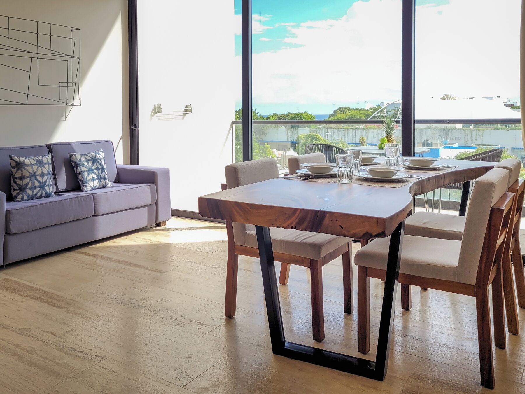 A modern living room with a sofa, dining table, and chairs. There is a large window with a view of the outdoors.