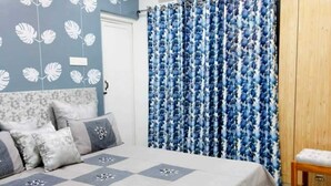 A bedroom with a bed, pillows, a blue floral curtain, and a wooden wardrobe.