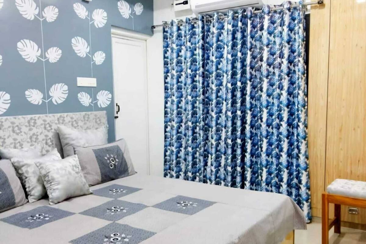 Ein Schlafzimmer mit einem Bett, Kissen, einem blumigen, blauen Vorhang und einem Holzschrank.
