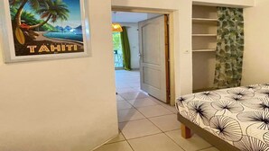 Un dormitorio con una cama, una puerta que da a otra habitación y un cuadro con una playa tropical.