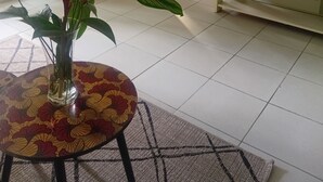 Una sala de estar con una mesa de comedor, un televisor sobre un mueble bajo, una cocina al fondo y un ventanal con cortinas.