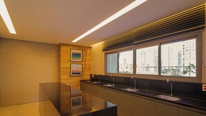 A modern kitchen with a long countertop, built-in sink, and a window with blinds. - Sunset Rooftop Studio - Comfort & Modernity in Brooklyn (Jardim das Acacias São Paulo)