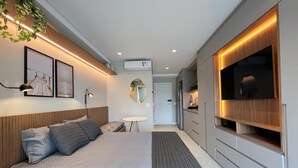 A modern bedroom with a bed, bedside tables, a TV, and a small table with a chair. - Sunset Rooftop Studio - Comfort & Modernity in Brooklyn (Jardim das Acacias São Paulo)
