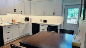 Een moderne keuken met witte kasten, een donker houten tafel en uitzicht op het buitenleven door een raam.