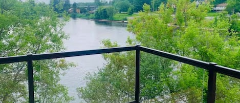 Una terraza de madera con barandal negro que da a un río rodeado de árboles.