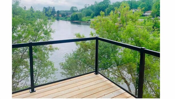 Een houten terras met een zwarte balustrade, met uitzicht op een rivier omringd door bomen.