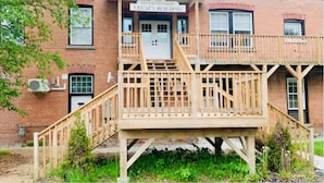 Een bakstenen gebouw met een houten terras en een trap die leidt naar een deur met de tekst 'Riverside Legacy Building'.