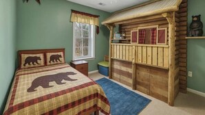 Ein Schlafzimmer mit einem Bett, das Bärenmotiven auf der Bettwäsche zeigt, einem hölzernen Spielhäuschen und einem Fenster mit Vorhängen.