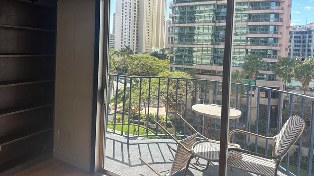 Un balcón con sillas de mimbre y una pequeña mesa, con vistas a un paisaje urbano con edificios altos y un jardín bien cuidado.