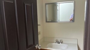 Un baño con tocador de madera, lavamanos blanco y espejo superior.