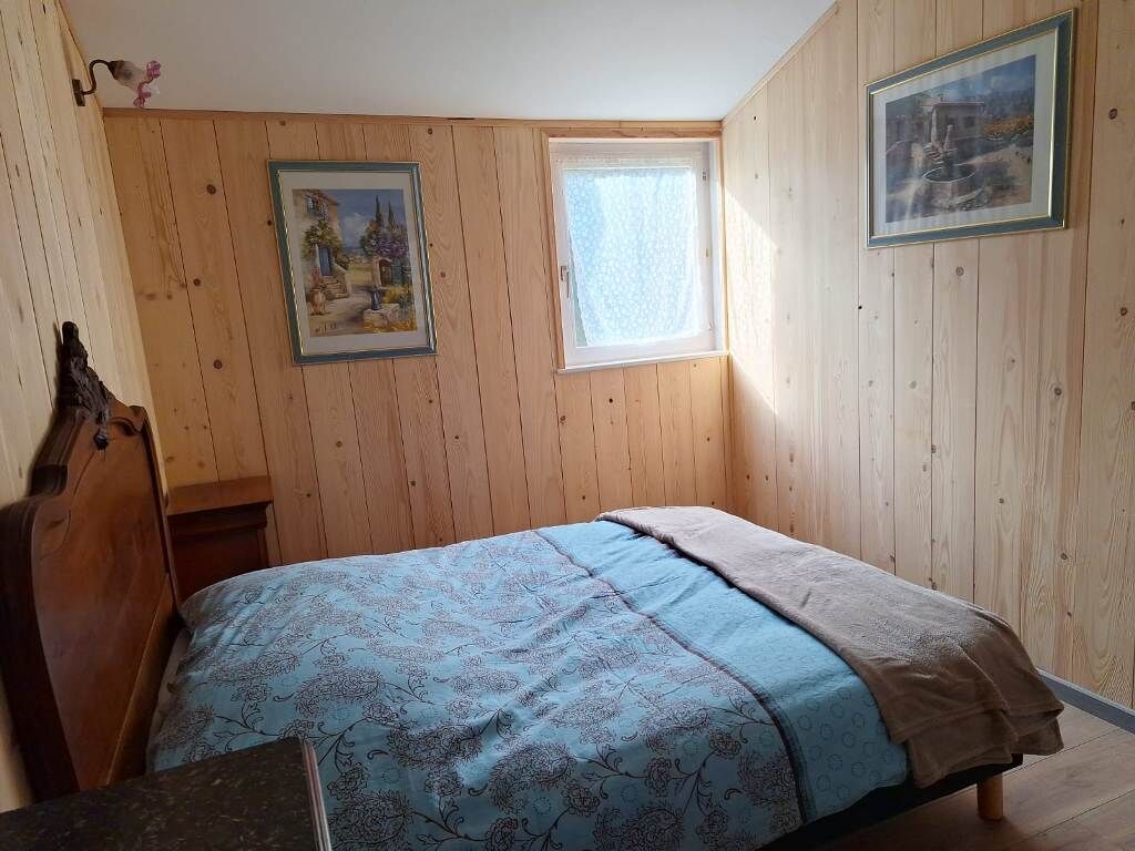 Une chambre avec des murs en bois, un lit recouvert d’une couvre-lit à motifs floraux, une fenêtre et deux tableaux encadrés.