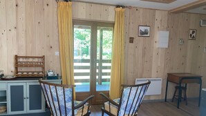 A wooden interior with a dining table, two chairs, a kitchen area with a stove, and a window with curtains. - The Kingfisher (Autrey)