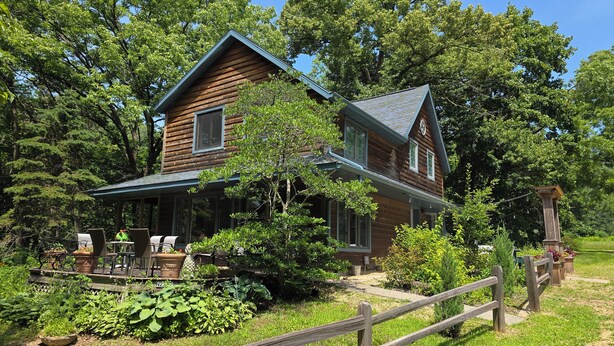 Une cabane en bois dotée d’un porche, entourée d’une végétation luxuriante et d’une clôture en bois.
