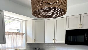 Una cocina moderna con armarios blancos, encimera negra, estufa de acero inoxidable y microondas negro.