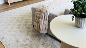 Una sala de estar moderna con un televisor de pantalla plana sobre un mueble de madera, un sofá gris, una mesa de centro redonda y una alfombra beige.