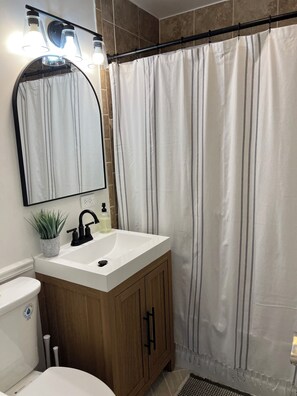 Une salle de bain avec un lavabo blanc, des meubles en bois, un miroir et un rideau de douche.