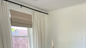 Un comedor con una mesa de madera, sillas negras, una vela y una ventana con cortinas.