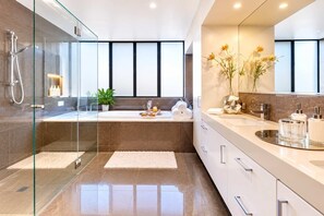 A modern bathroom with a glass-enclosed shower, a large mirror, a bathtub, and a vanity with toiletries.