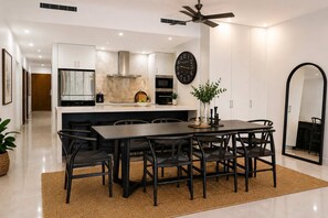 A modern kitchen with white cabinets, a stainless steel range hood, and a black clock on the wall.