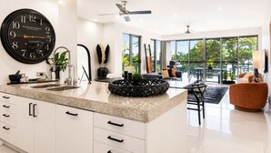 A modern kitchen with a large clock, white cabinetry, and a dining area with a view. - Beachfront Bliss in Townsville on The Strand 3BR Pool and Parking (North Ward)