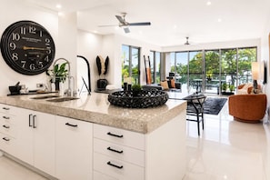 A modern kitchen with a large clock, white cabinetry, and a dining area with a view.