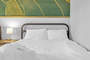 Ein ordentlich bezogenes Bett mit weißen Leinentüchern, einer Nachttischlampe und einem Wandbild über dem Bett.
