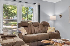 A living room with a brown leather sofa, a side table with a book, and a lamp on a wooden side table.