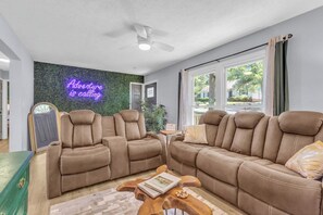 Ein Wohnzimmer mit zwei braunen Sofas, einem Holztisch und einem Neon-Leuchtschild an der Wand.