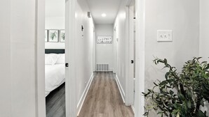 Un pasillo estrecho con suelo de madera, paredes blancas y una cama a la izquierda.