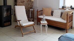 Ein gemütliches Wohnzimmer mit einer Steinwand, einem schwarzen Holzofen, einer Holzsofa und einem weißen Sessel.