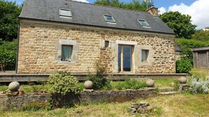 Ein Steinhaus mit schrägem Dach, zwei Fenstern und einer Tür.