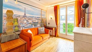 A room with a view of the Eiffel Tower, a wooden floor, a sofa, a lamp, and a window with curtains.