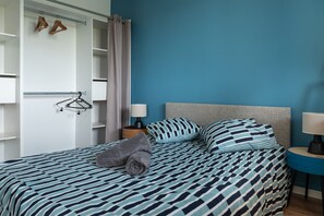 A bedroom with a bed, a wardrobe, a nightstand, and a lamp.