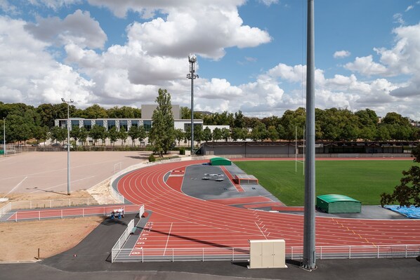 A running track with a red surface, a green field, and a building with a modern design in the background.