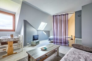 A modern living room with a dining area, a TV, a window, and a bed. - Le Nid Marin - A 400m de la plage (Saint-Aubin-sur-Mer)