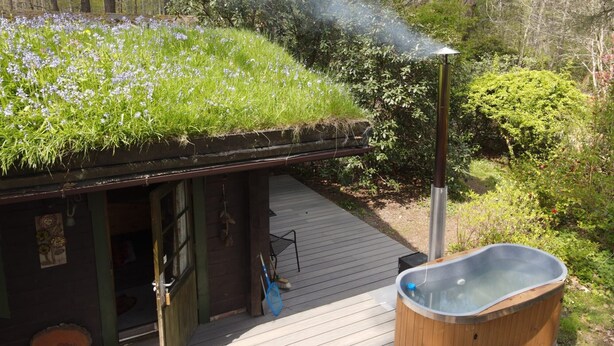 Una baita di legno con tetto verde, vasca idromassaggio e veranda in legno.