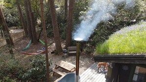 Una vasca idromassaggio su un pontile di legno, con uno scarico che emette vapore, circondata da alberi e da una zona erbosa.