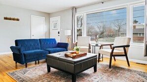 A living room with a blue sofa, a dark ottoman, and a beige armchair. - Homewood Oasis with 3 Beds and A Fully Fenced Backyard! (Homewood)