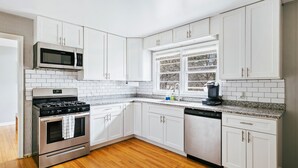 A modern kitchen with white cabinets, a stainless steel stove, a microwave, and a window with a view of trees. - Homewood Oasis with 3 Beds and A Fully Fenced Backyard! (Homewood)