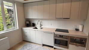 Een moderne keuken met witte kastjes, een grijze vloerkleed en een raam met uitzicht op groen.
