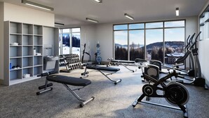 Een moderne sportschool met cardioapparatuur, gewichtbanken en een groot raam met uitzicht op de bergen.
