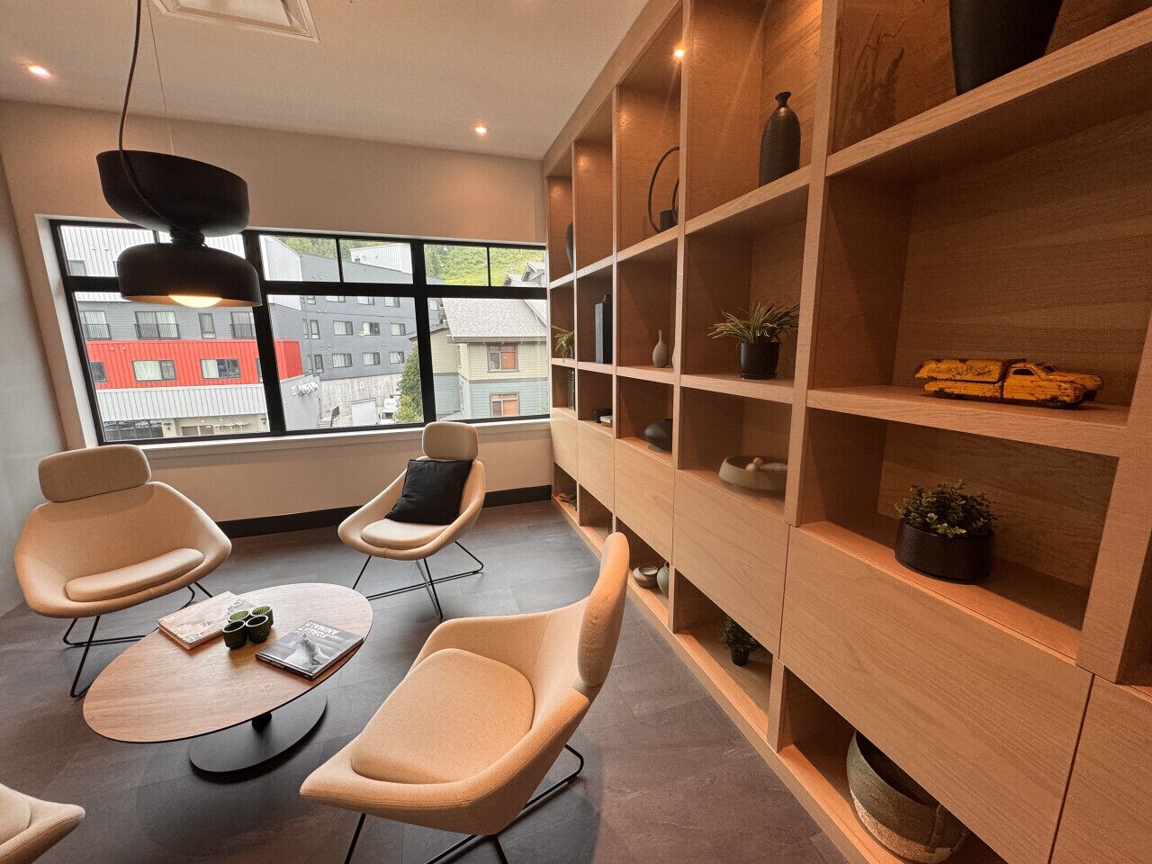 A modern interior with two beige chairs, a wooden coffee table, and a built-in wooden shelving unit with decorative items.